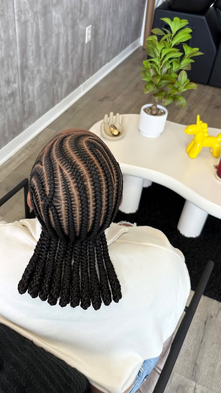 Thick patterned cornrows gathered into long braids in a salon chair