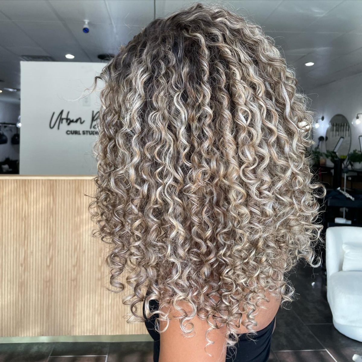 Shoulder-length curly ombré hair with darker roots and lighter ends in a salon