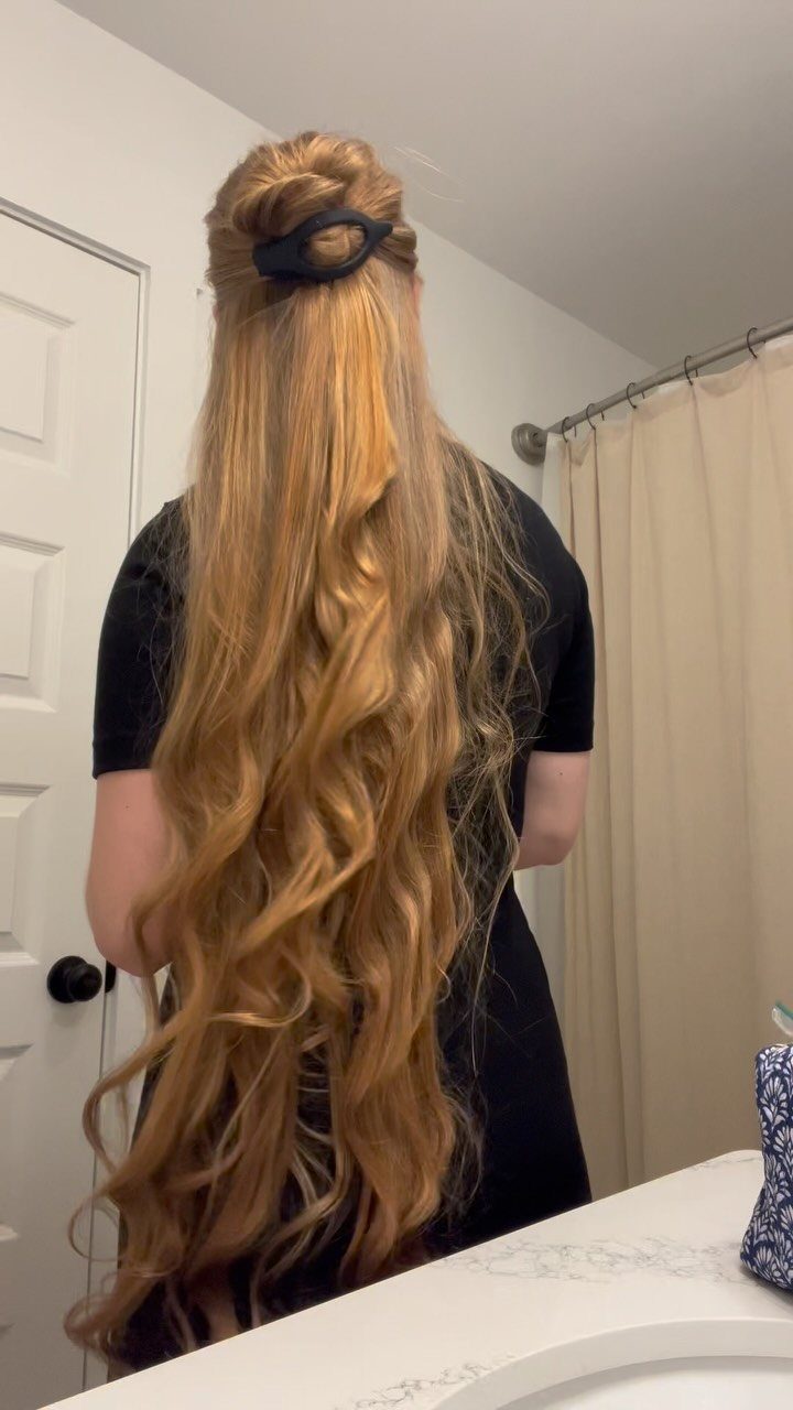 Long blonde hair styled half-up with a black clip and loose curls