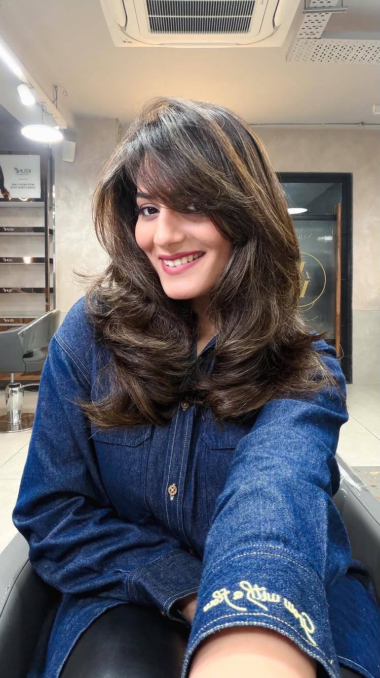 Woman with long dark curls and a side-swept bang posing in a salon