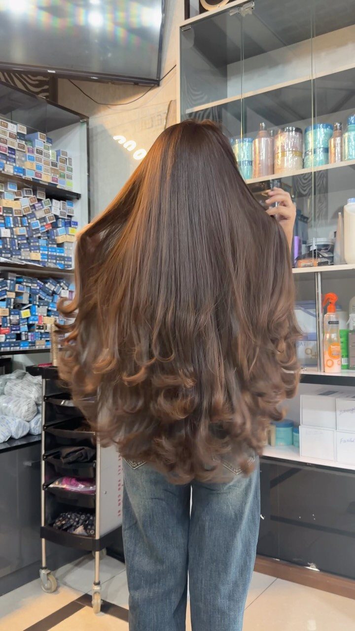 Long brown hair falls in glossy, gentle curls down the back