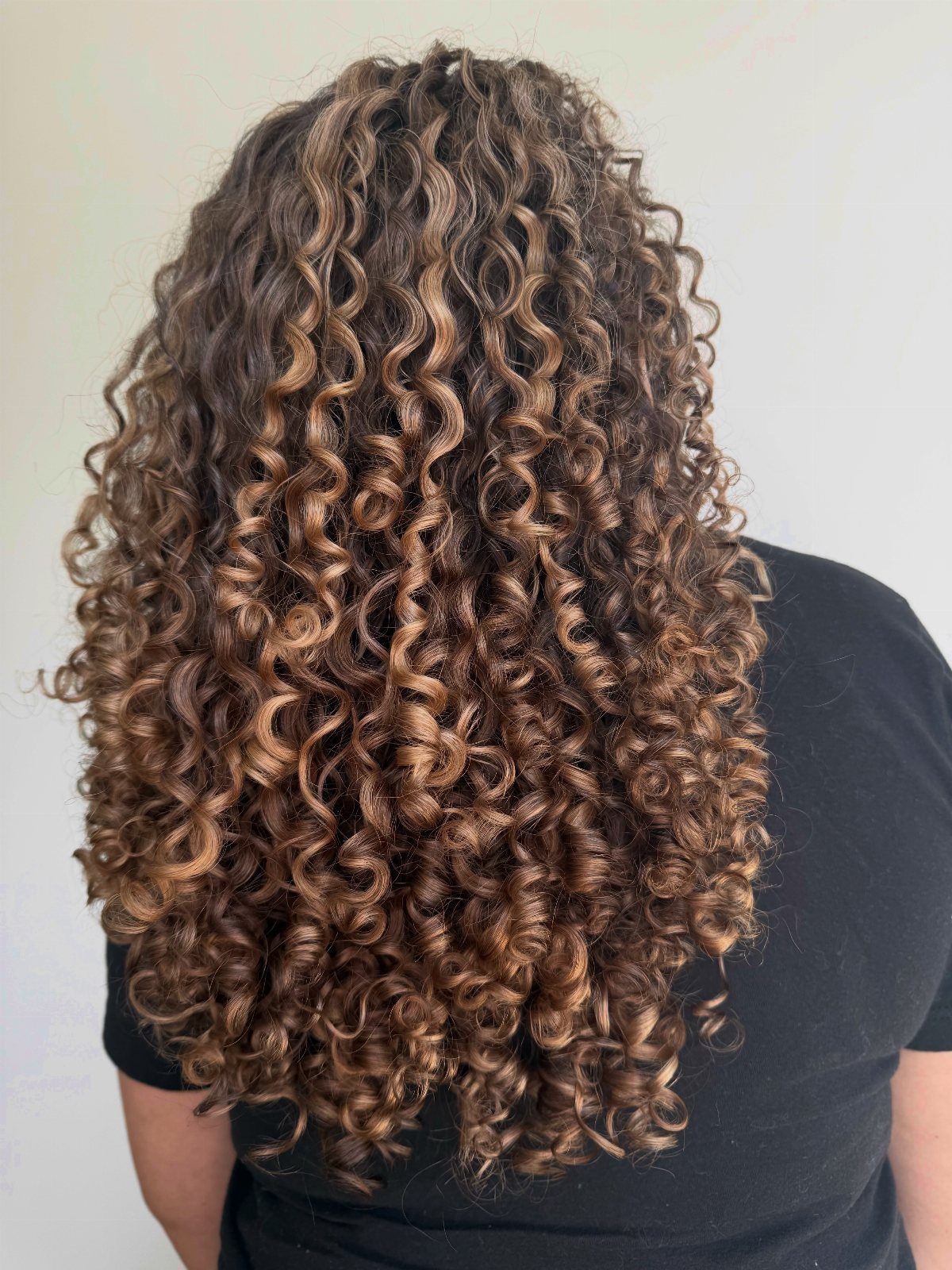 Long natural brown curls cascade down the back over a black top