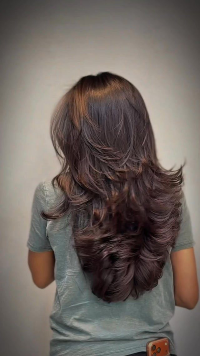 Long dark hair with voluminous shorter layers over curled lengths, seen from behind
