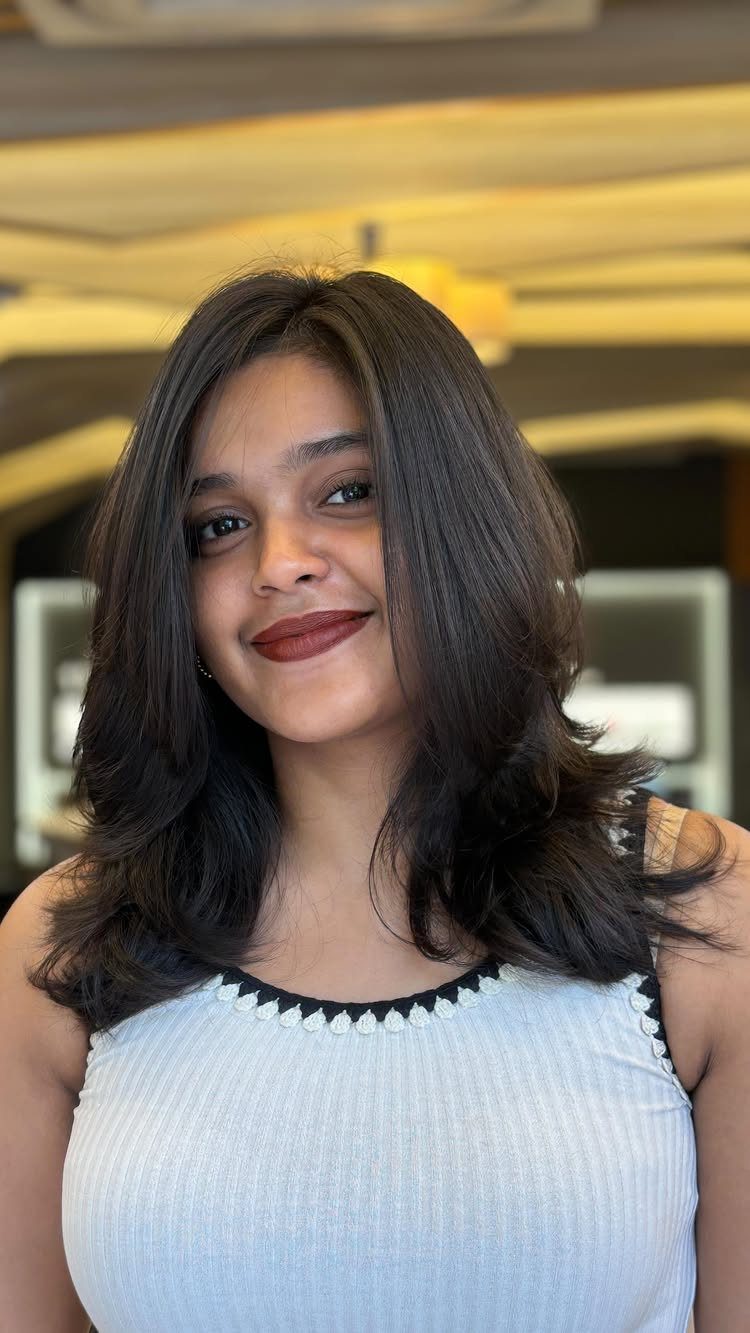 Woman showing dark face-framing layers blended into long, softly curled hair