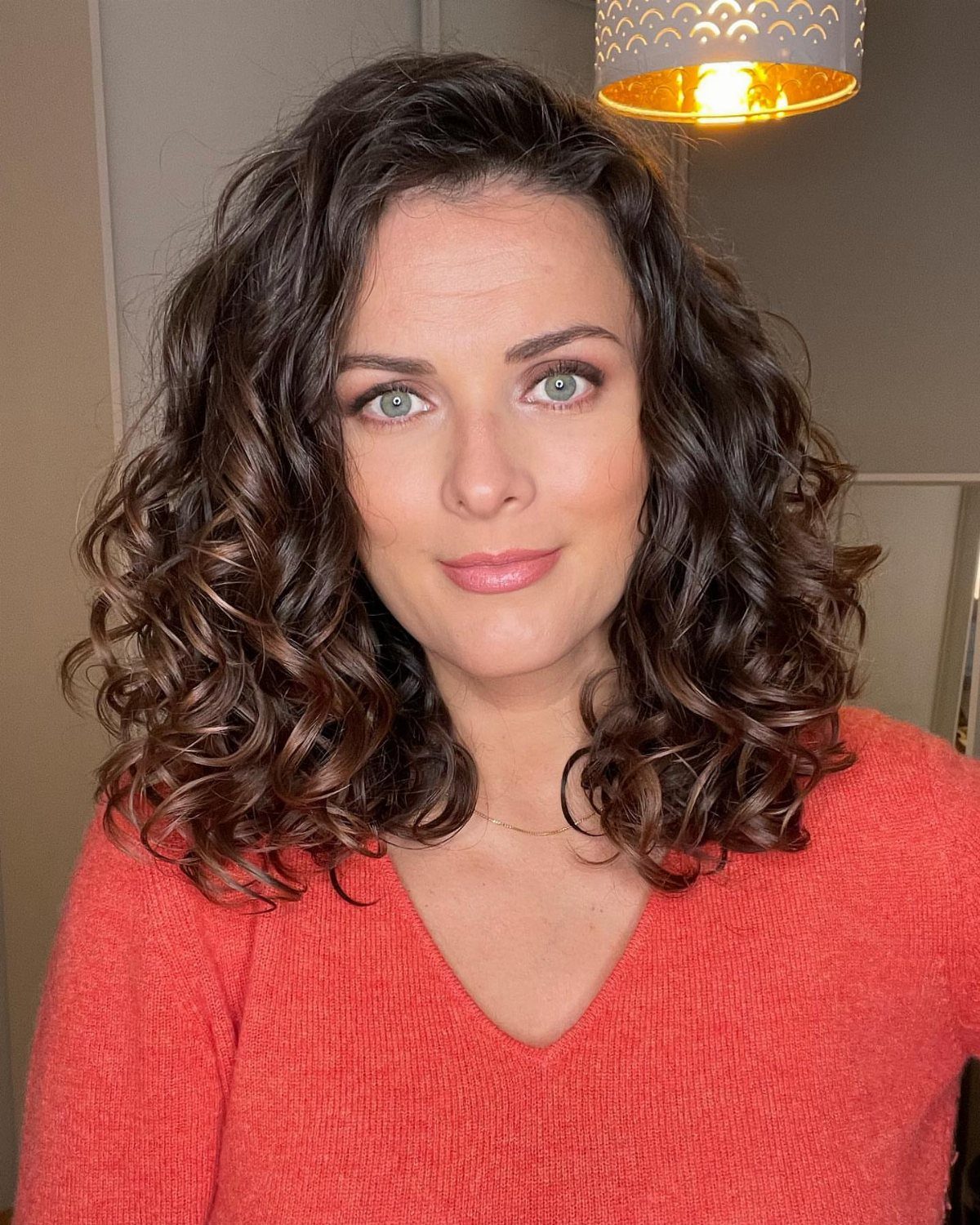 Woman with shoulder-length dark curls wearing a coral-red sweater