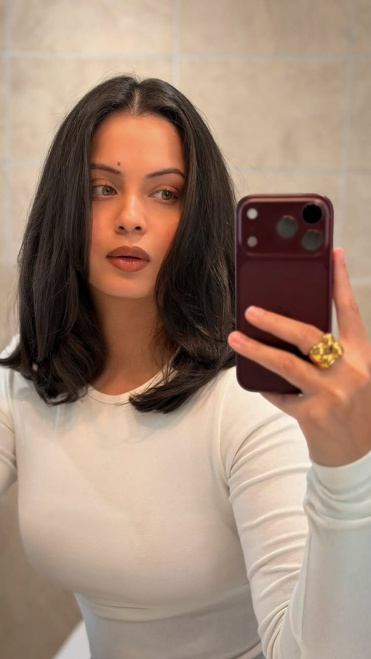Woman showing shoulder-length dark layered hair in a mirror selfie