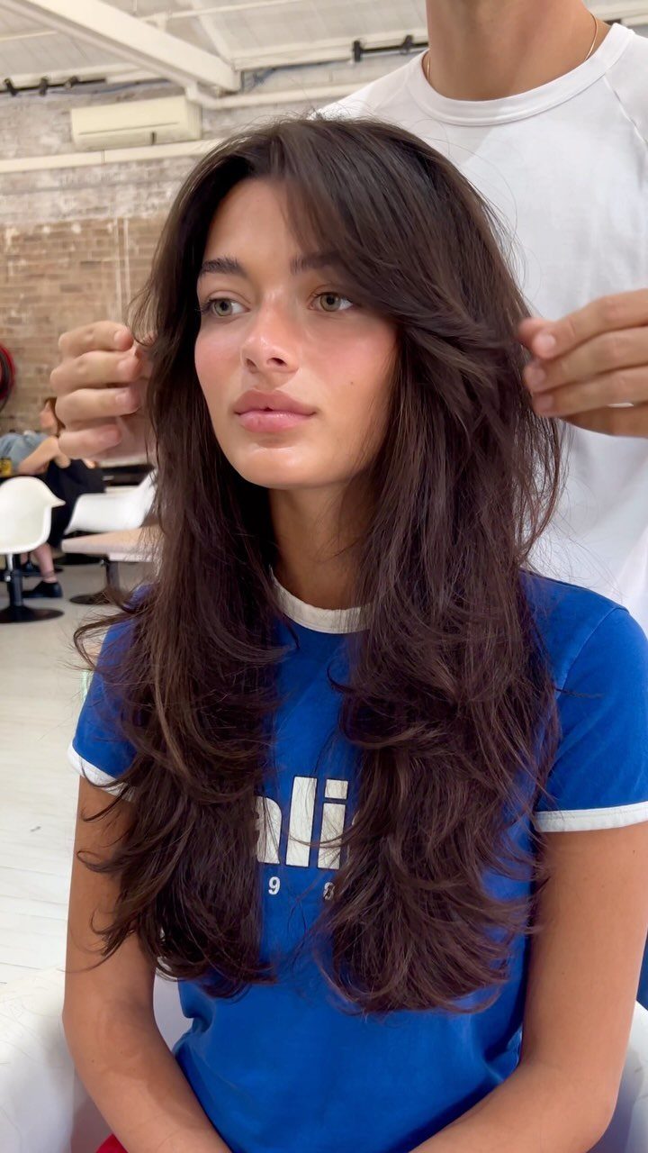 Young woman showing long dark layered hair with soft face-framing pieces in a salon