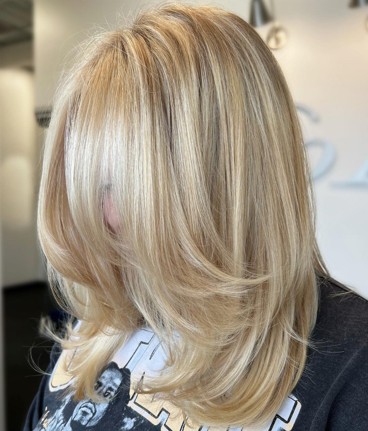 Blonde layered haircut with swept curtain bangs and feathered ends
