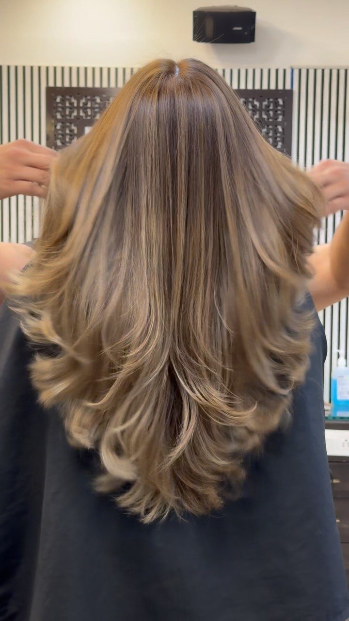 Long highlighted brown hair with feathered layers is spread out by hands