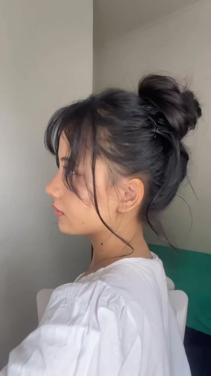 Woman with dark hair in a loose high bun and wispy face-framing strands