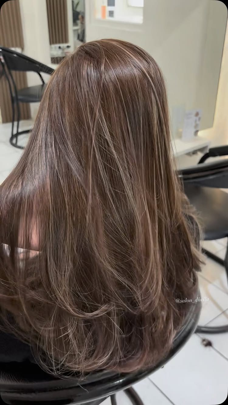 Long brown hair falls in softly layered lengths over a black salon chair