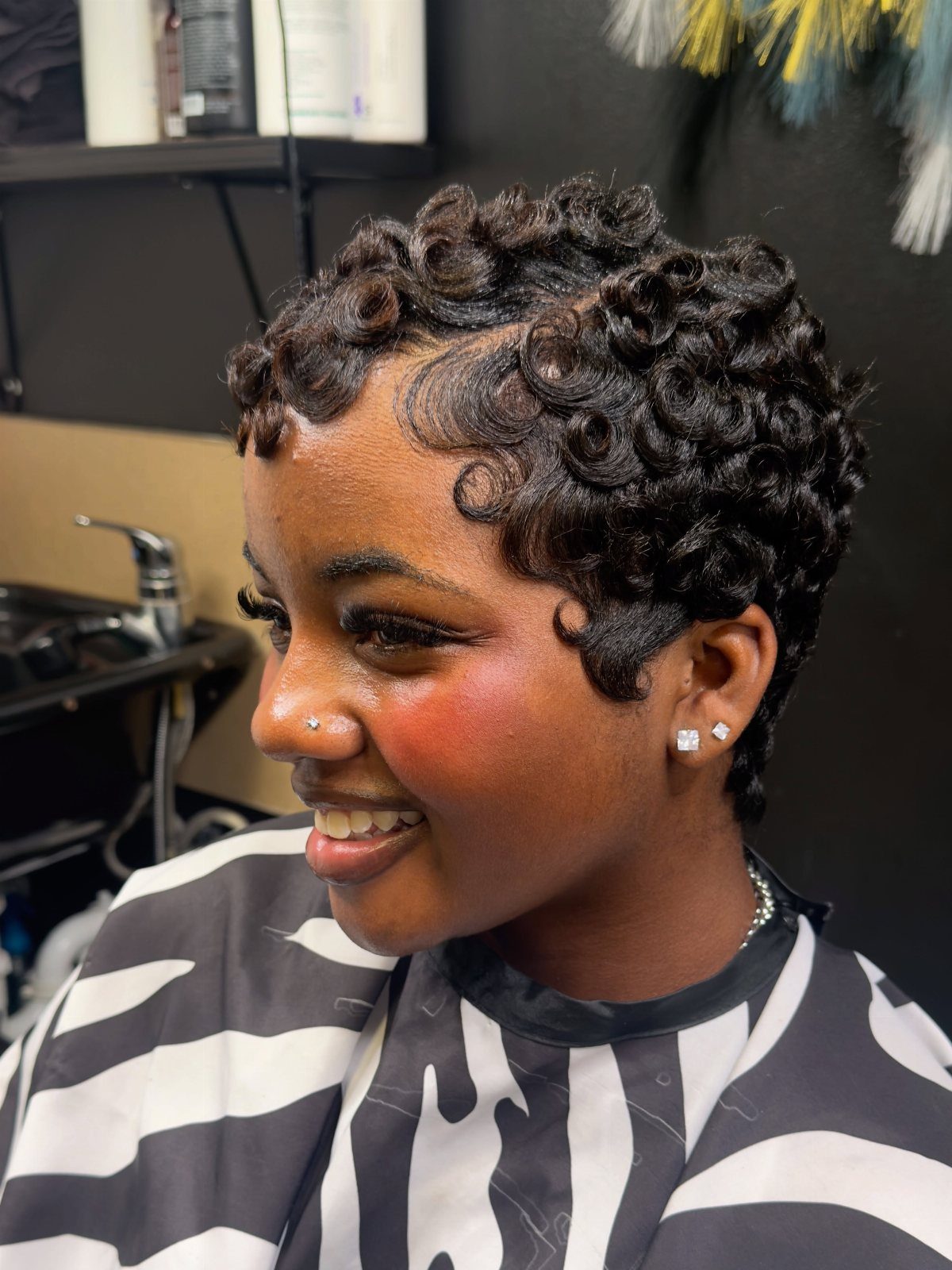 Woman showing a short curly pixie haircut with defined crown curls in a salon