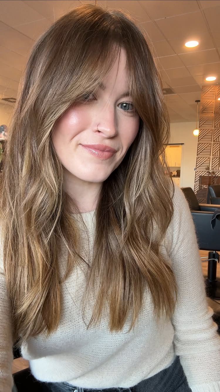 Woman with long wavy brown hair and cheek-framing curtain bangs