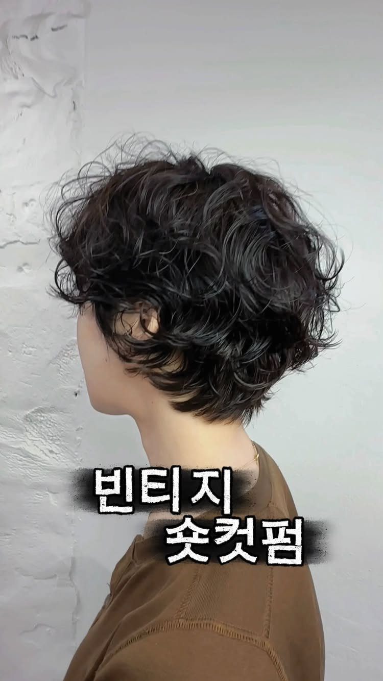 Side-profile person showing short, tousled dark messy waves against a textured light wall