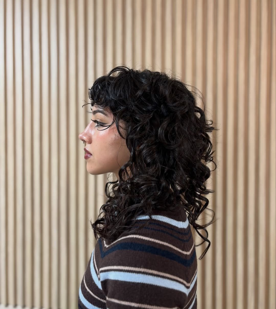 Profile showing dark curly shag haircut with short bangs and graduated layers