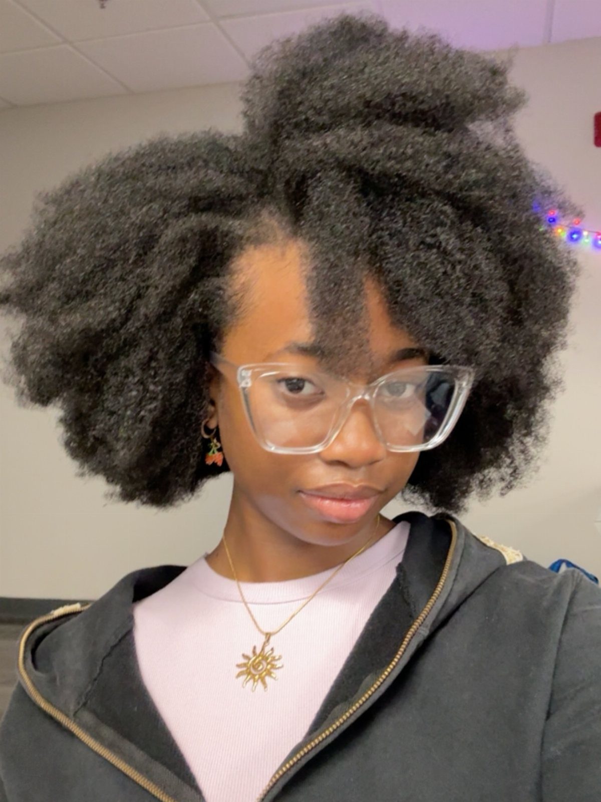 Person wearing a full natural afro with clear glasses and a dark jacket