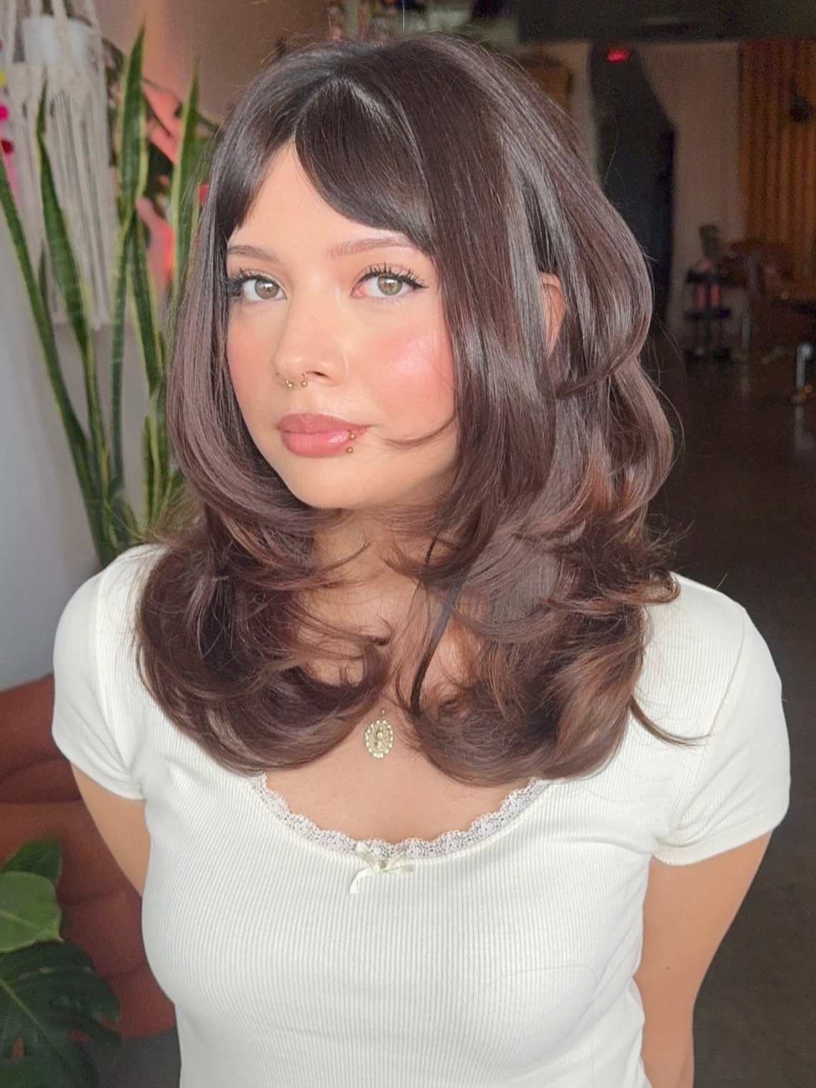 Woman with layered shoulder-length brown hair, face-framing bangs, and curled ends
