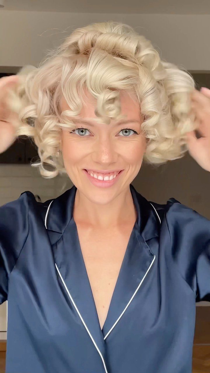 Woman adjusts short blonde curls while wearing a navy satin robe