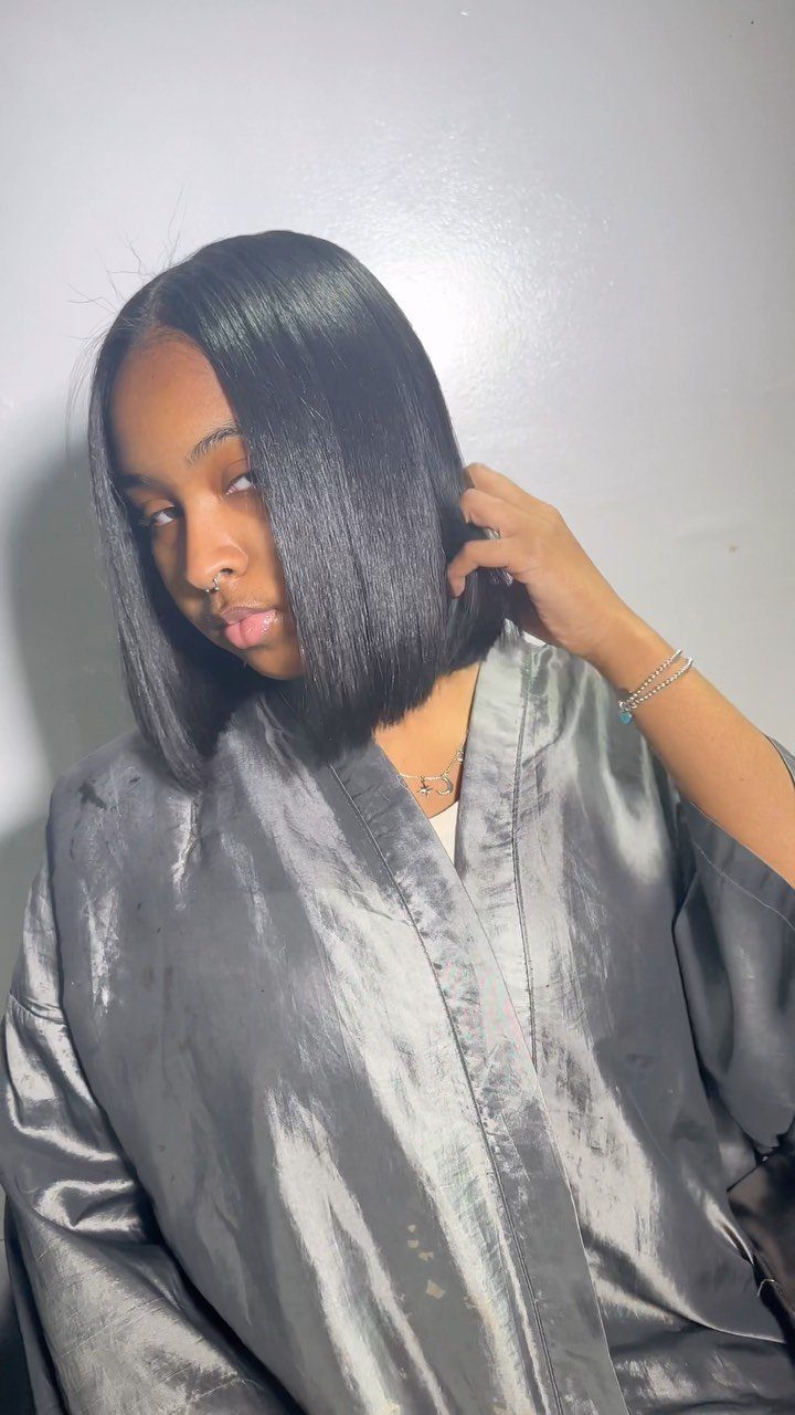 Woman with sleek, straight black bob and side part touching her hair