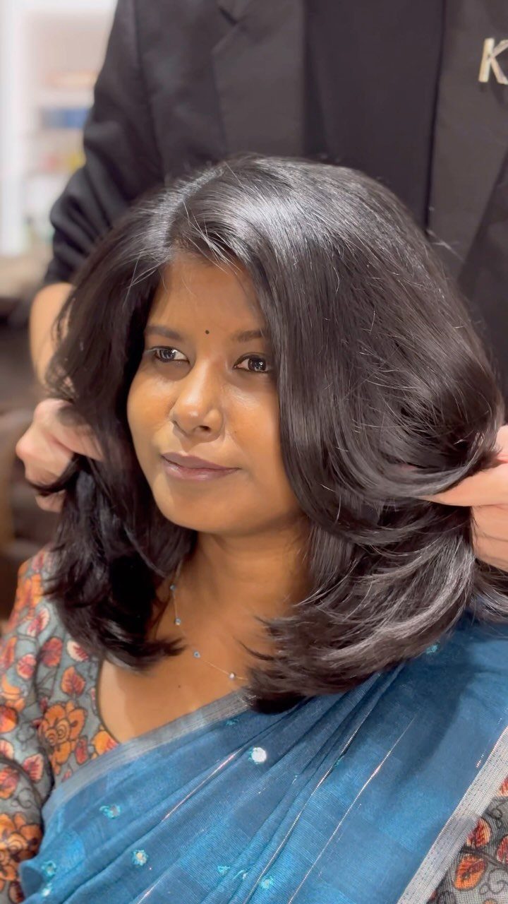 Woman showing glossy shoulder-length hair with soft, voluminous layered ends in a salon