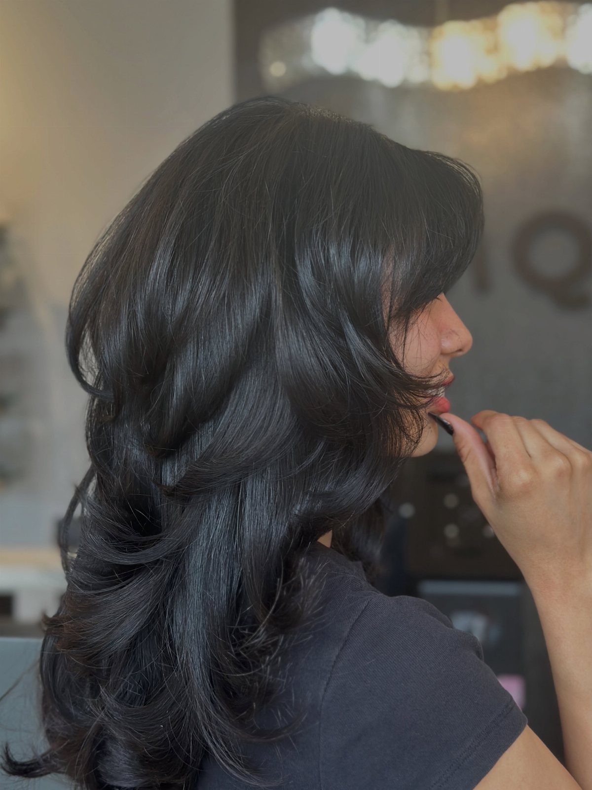 Long dark layered hair with voluminous curled ends shown in profile