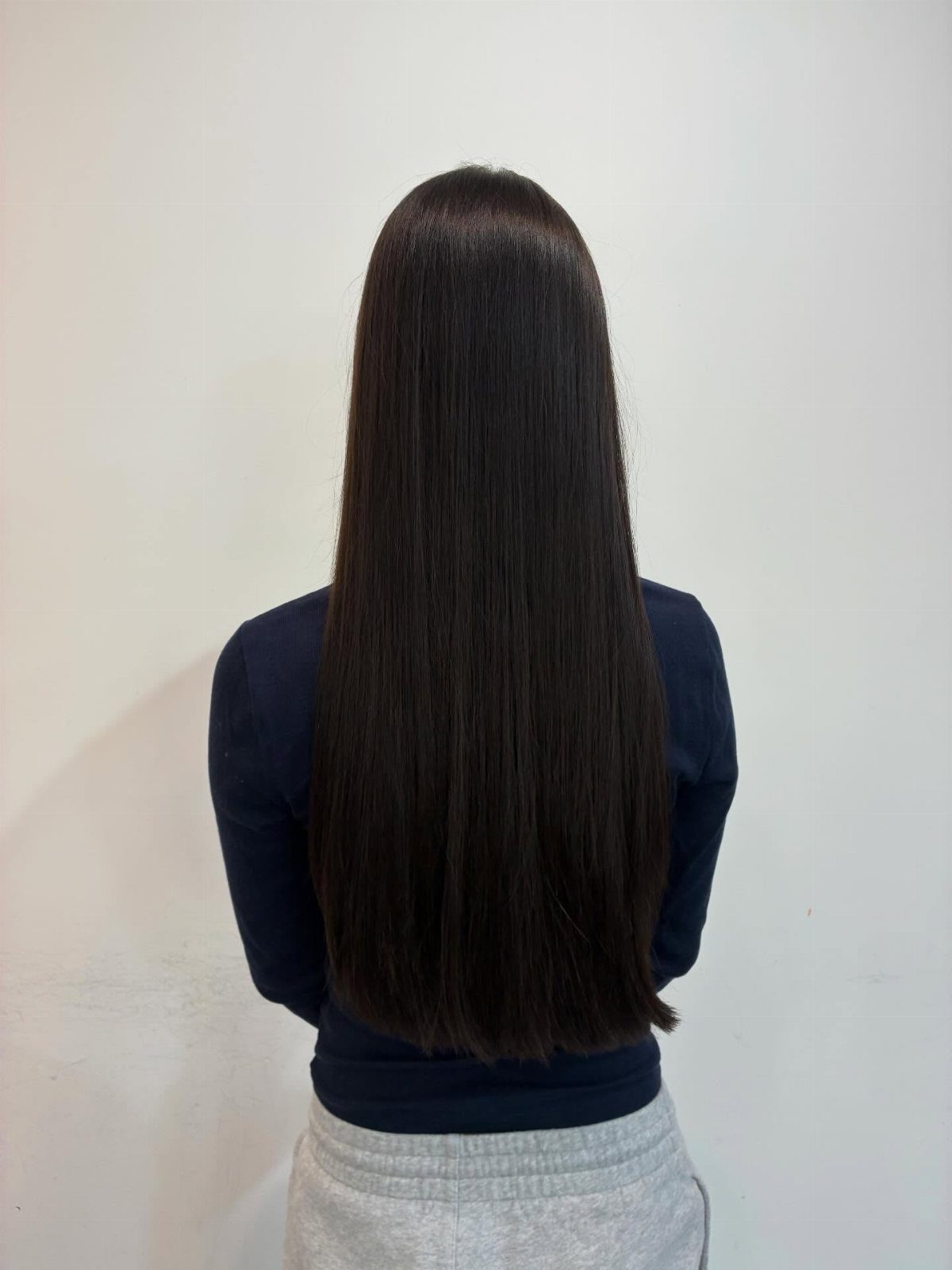 Long straight dark hair with an even blunt bottom line against a plain wall
