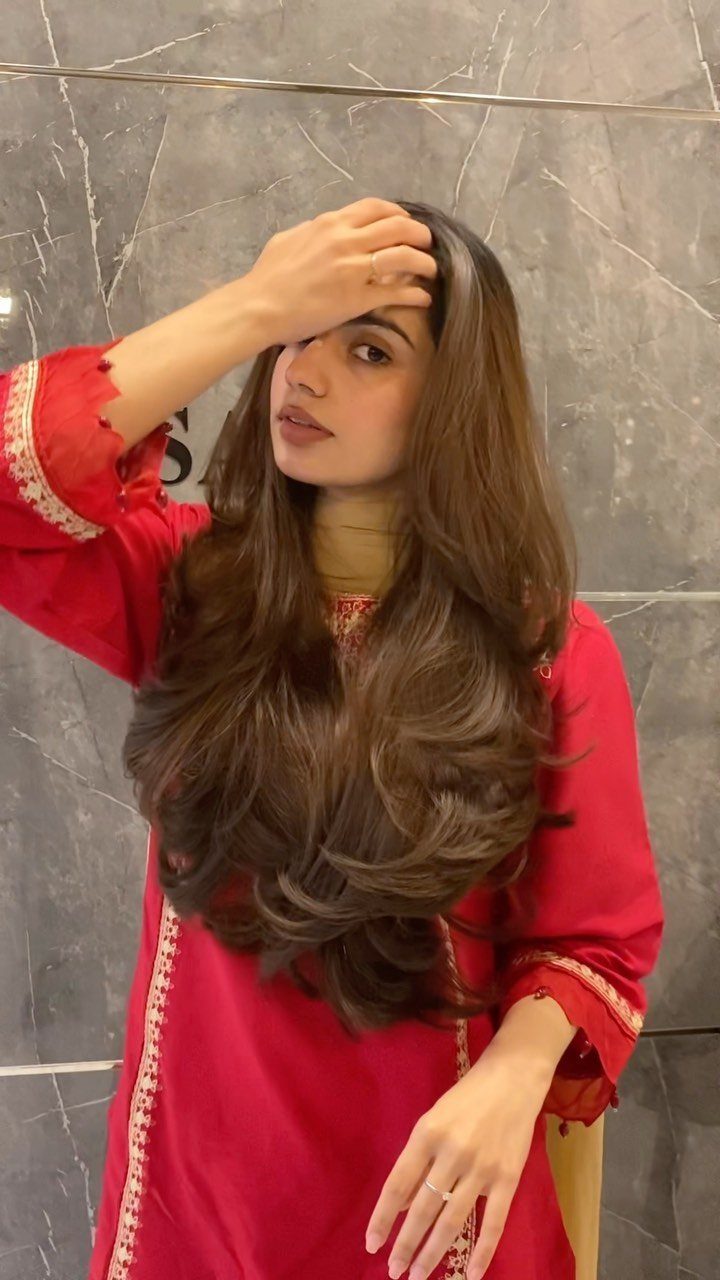 Woman with center-parted, long brown layered hair in a red outfit
