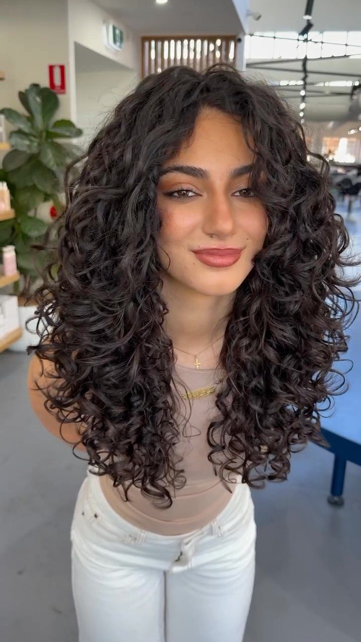 Woman displaying long, dark layered curly hair with voluminous defined ringlets