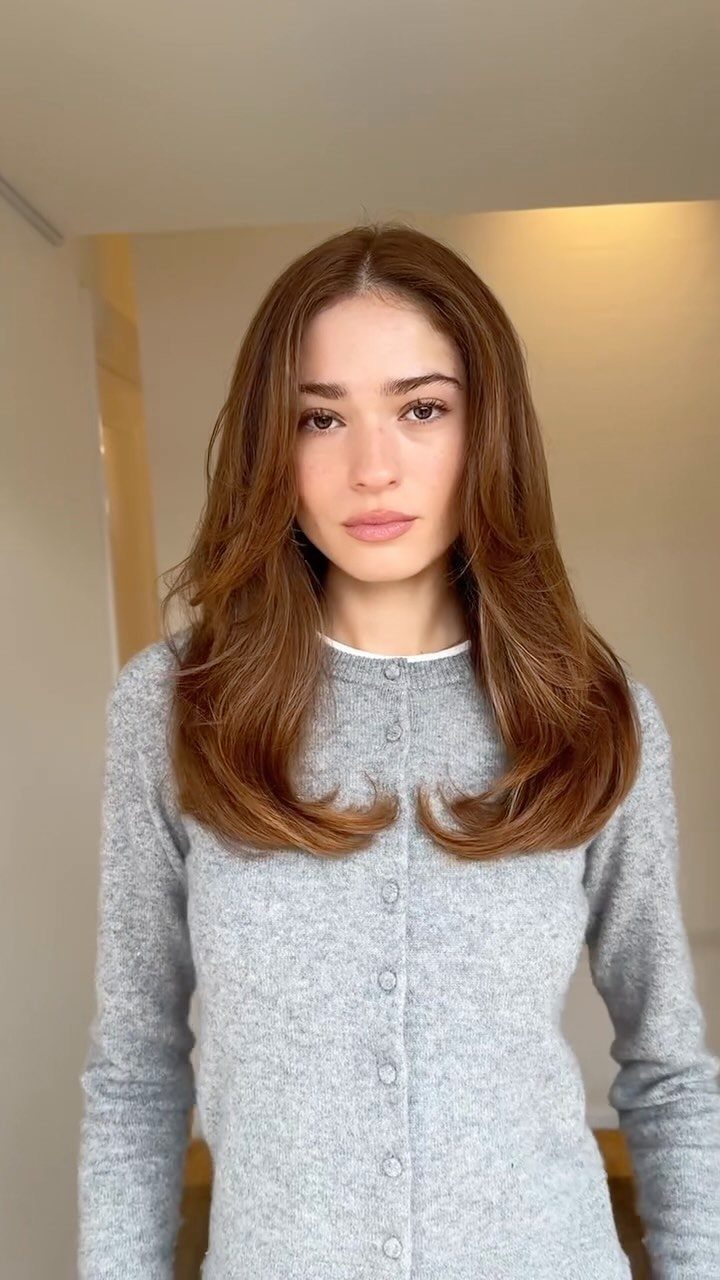 Woman showcasing long softly layered brown hair with curled ends indoors