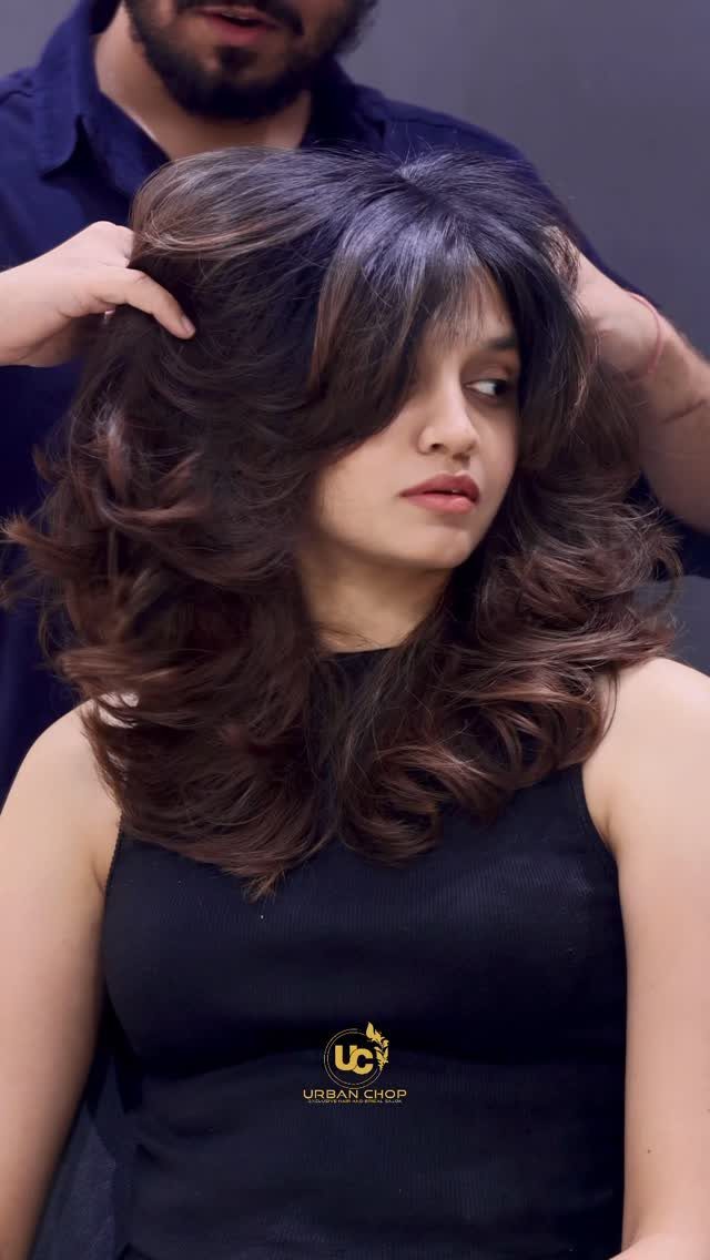 Woman displaying long dark hair with voluminous soft feathered layers in a salon