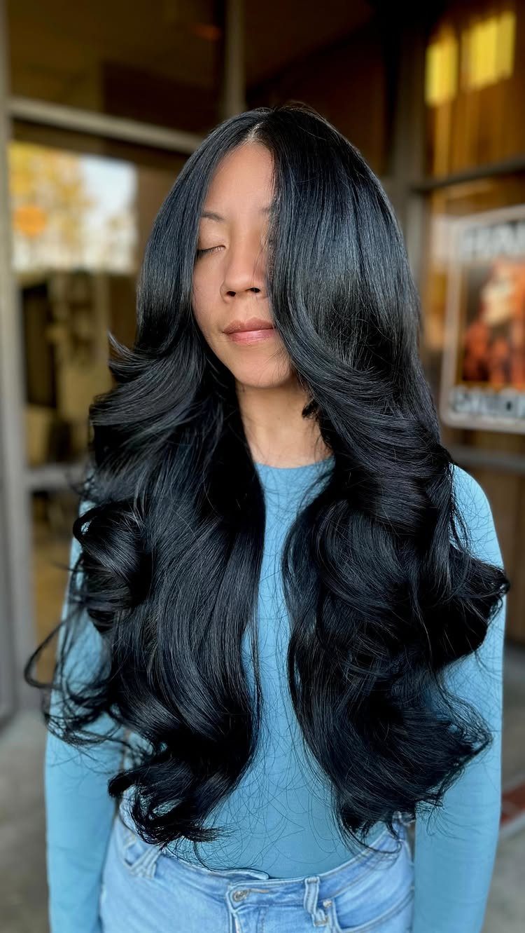 Long black graduated layers fall in voluminous curls over a light blue top.