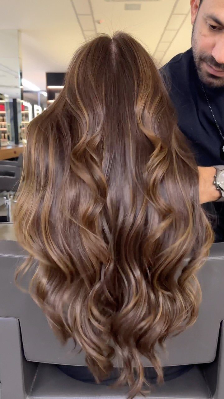 Long highlighted brunette layers cascading in loose curls down a salon client's back