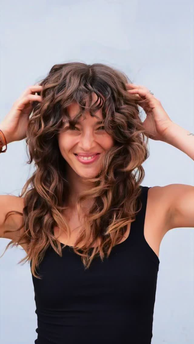 Woman tousles long, mixed-length brown layers with curly curtain bangs
