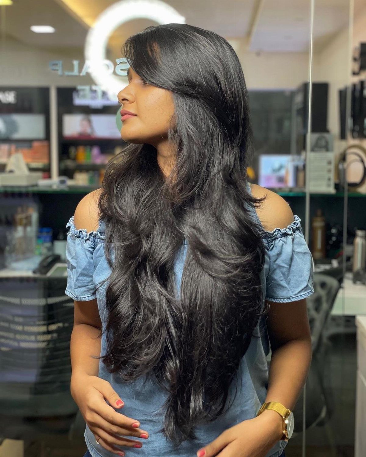 Woman with long glossy layered black hair and sweeping side bangs in a salon.