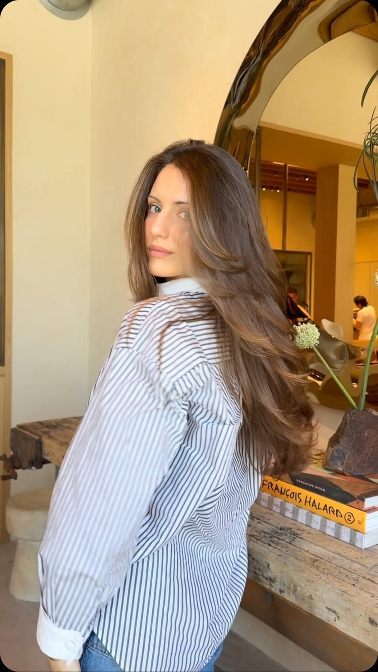 Woman showing long, smooth brunette layers with softly curved ends in a salon