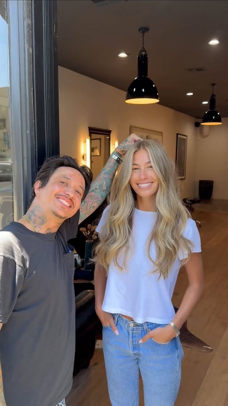 Woman showing long blonde face-framing layers beside a smiling man in a salon
