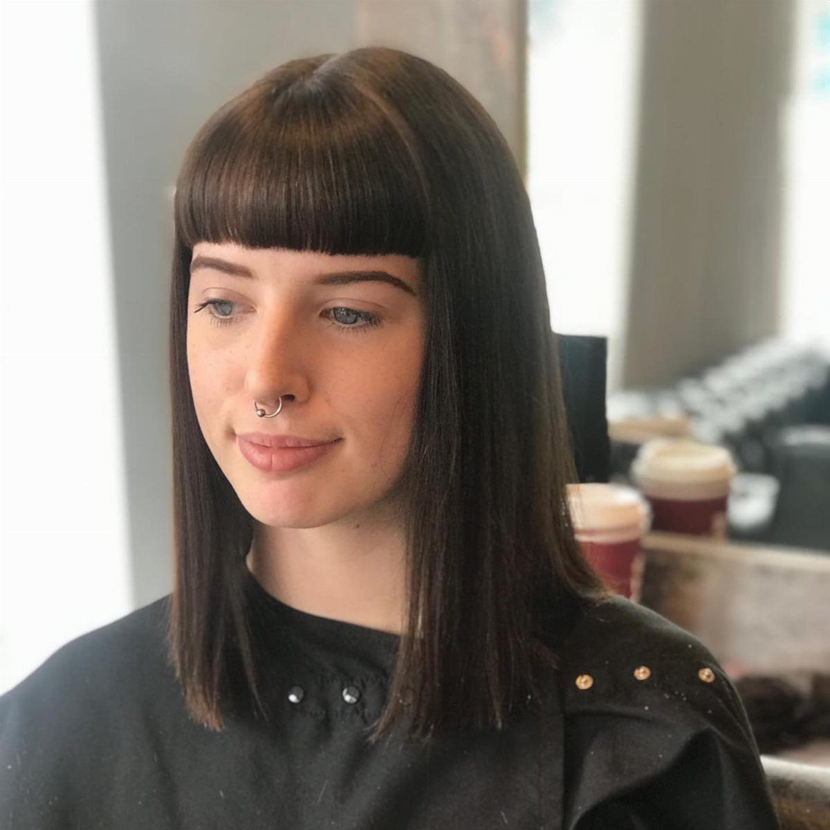 Person with straight dark hair and a sharply cut, full blunt fringe in a salon