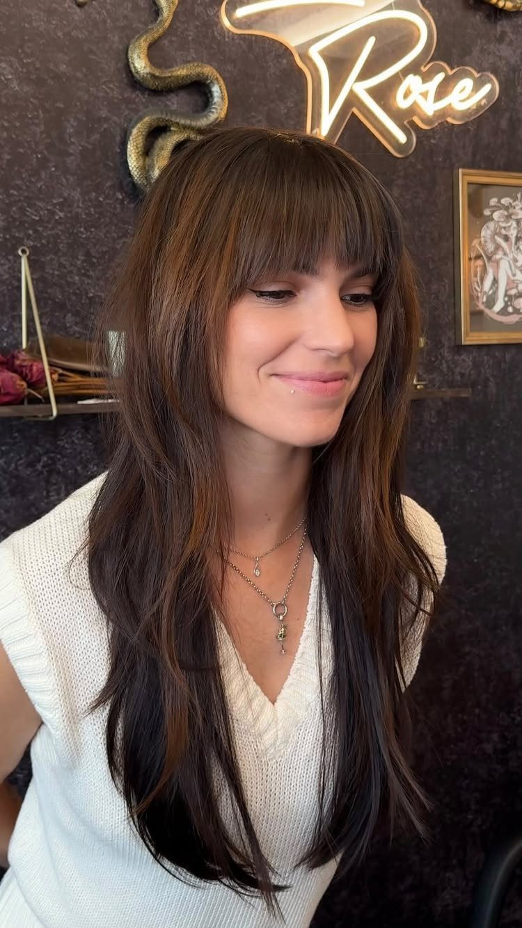 Woman with long, layered dark hair and blunt bangs in a salon