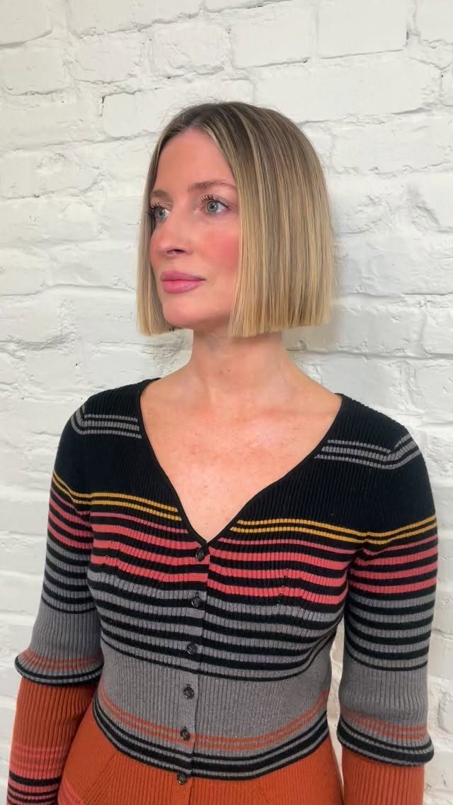 Woman showcasing a straight chin-length blonde bob haircut against a white brick wall