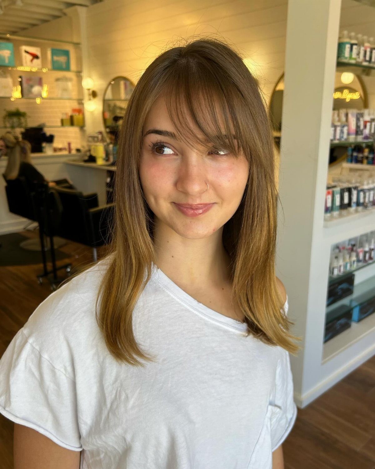 Woman with straight light brown hair and side-swept bangs in a salon