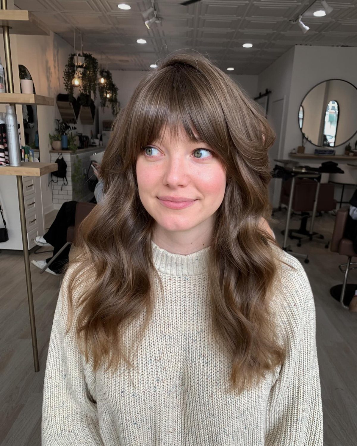 Woman with wispy center-parted bangs and voluminous long waves in a salon
