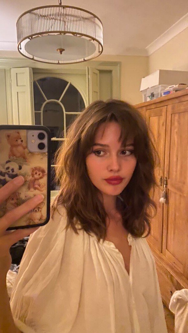 Woman with long wavy brown hair and soft, parted Birkin bangs