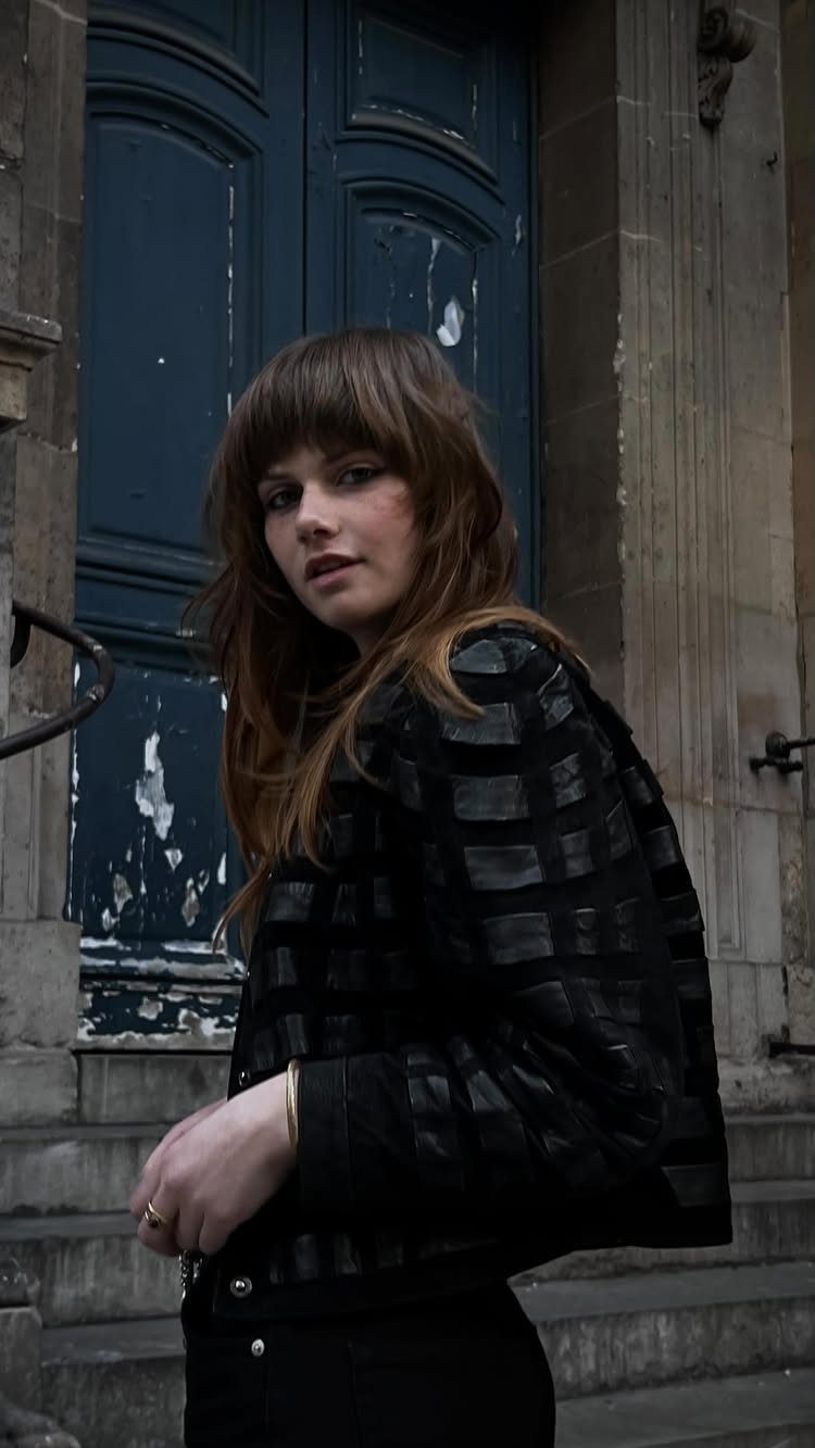 Woman with long brown hair and eye-skimming bangs standing before a blue door
