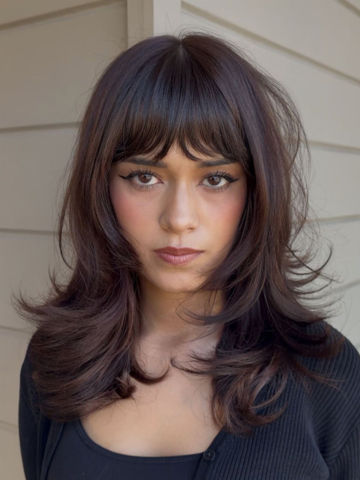 Woman with long layered dark hair and a full fringe wearing a black top