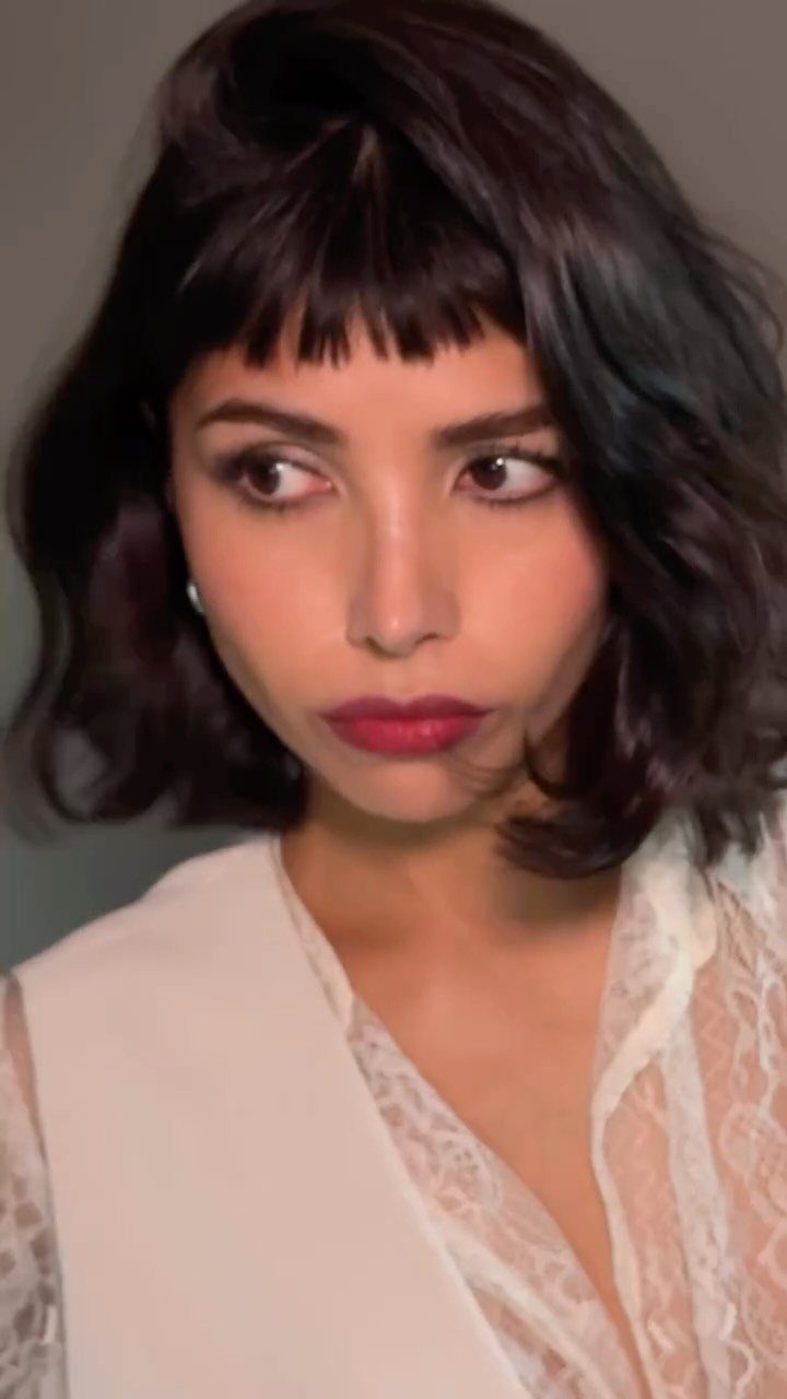 Woman with dark wavy hair and short bangs above her eyebrows