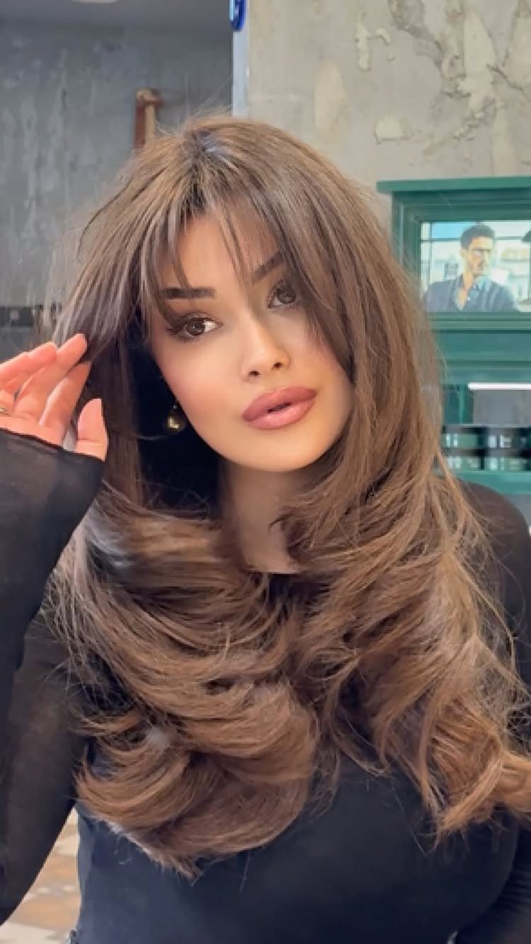 Woman with long layered brown hair and airy wispy bangs in a salon