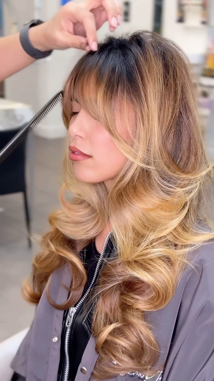 Woman with long, voluminous layered hair and curled blonde ends in a salon