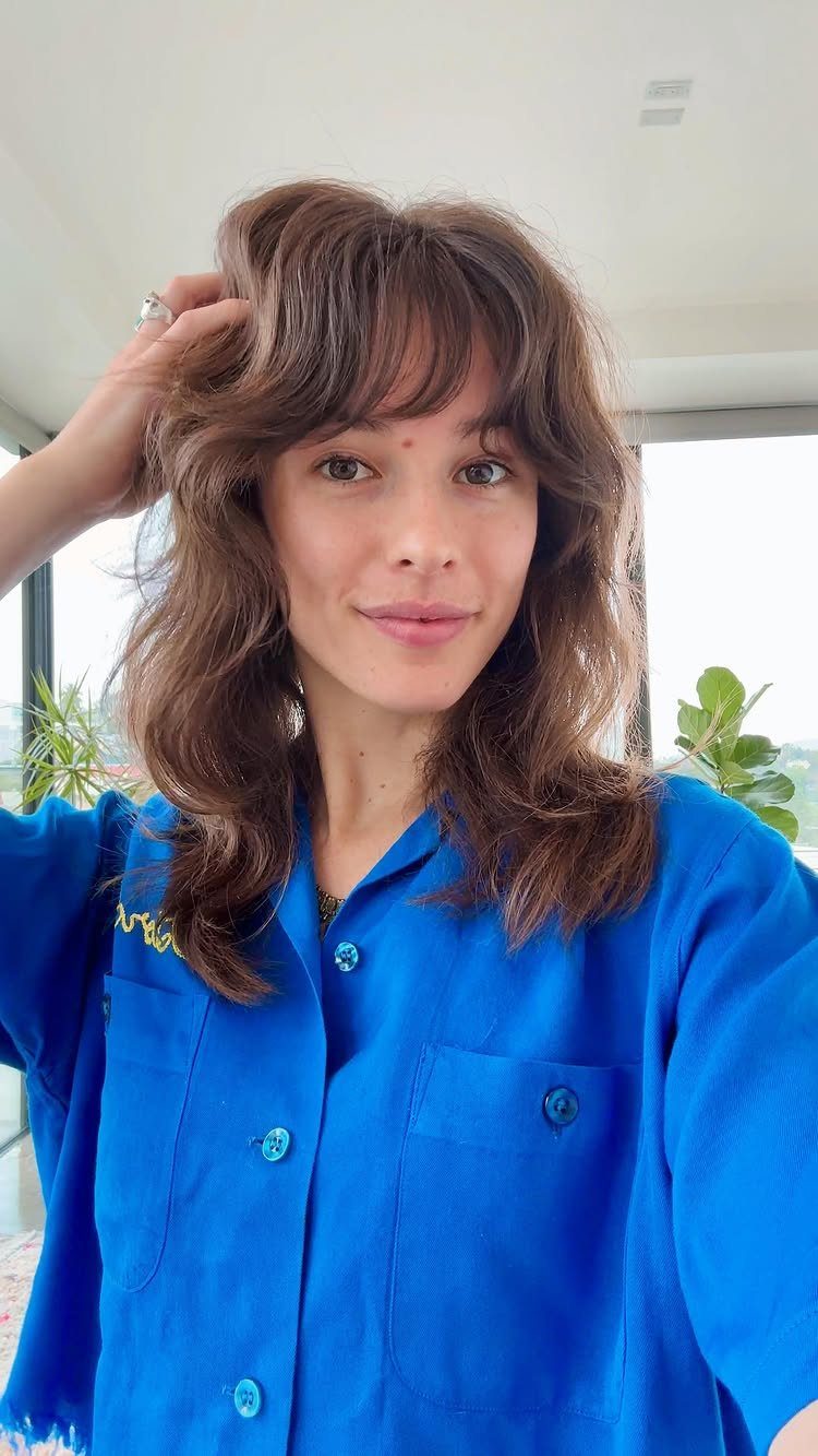 Woman with long wavy brown hair and soft, full Birkin bangs