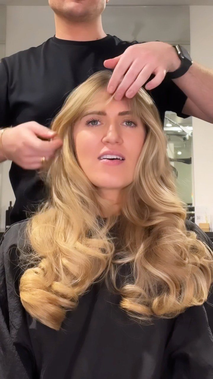 Woman with long blonde layered curls and light bangs in a salon chair