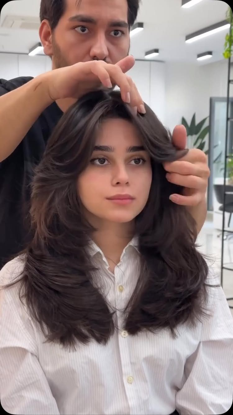 Woman displays a voluminous layered haircut with long face-framing bangs in a salon